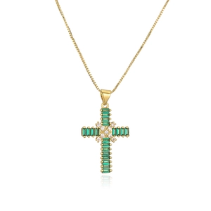 Macro detail of gold-plated cross pendant with green emerald and sparkling zircons