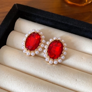 Macro shot of red oval gemstone earrings with white pearl border in a beige velvet jewelry box