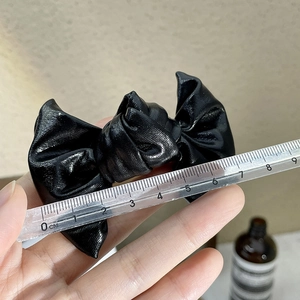 Detail view showing a black metallic leather bow hair clip measuring 9cm with a clear ruler