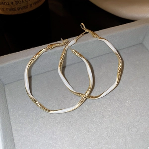Detailed macro view of large irregular gold earrings with white enamel and hammered texture