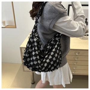 Detail view of denim crossbody bag featuring black and white checkerboard pattern and tassels