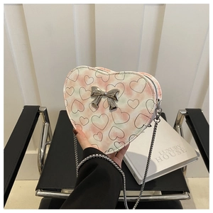 Detail view of heart-shaped crossbody bag with bow accent and chain strap held by hand