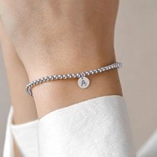 Détail d'un bracelet en perles argentées avec un pendentif rond gravé de la lettre A