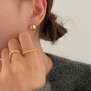 Close-up of minimalist gold ball earrings and textured rings paired with grey knitwear