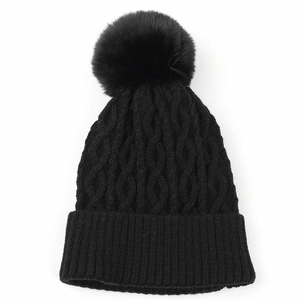 Dettaglio berretto nero in maglia a trecce con grande pompon in pelliccia sintetica