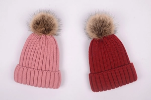 Detailed close-up of pink and red knit beanies with fluffy faux fur pom-poms on top