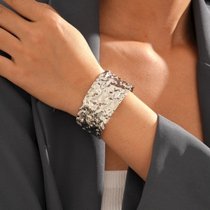 Dettaglio del bracciale rigido in metallo argentato strutturato al polso su sfondo grigio