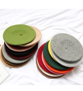 Flat lay of colorful wool beret hats in various shades on white wrinkled fabric