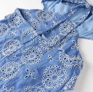 Detail of blue midi dress showing intricate floral eyelet embroidery and neckline ties