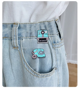 Detail shot of vintage camera and phone enamel pins on white clothing