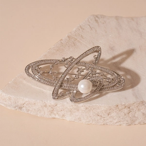 Detailed close-up of a silver Saturn brooch with zircons and central pearl on a stone