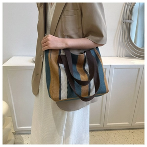 Detailed view of large striped canvas tote bag with brown woven shoulder strap on model