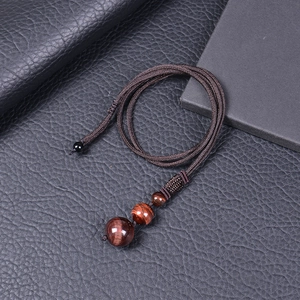 Macro detail of the dark brown braided cord and three polished red tiger eye beads