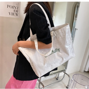 Detail of a large white canvas tote bag with a clear PVC layer and green lettering text