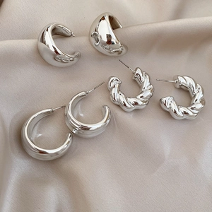 Close-up of three pairs of silver C-shaped and twisted metal hoop earrings on silk cloth