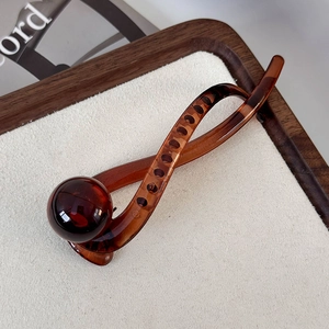 Detailed view of coffee-colored resin hair claw clip with round ball on wooden tray