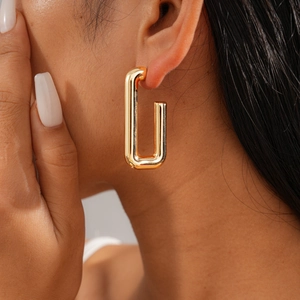 Close-up of a model wearing minimalist geometric gold rectangular stud earrings with a glossy finish