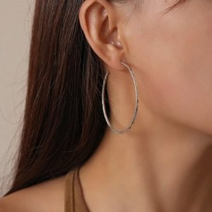 Macro detail of large matte silver hoop earrings with a textured sparkling finish on model