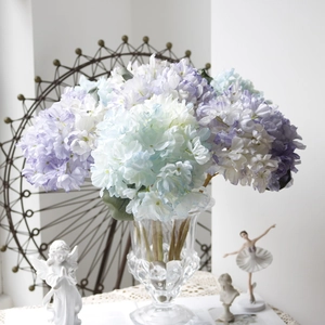 Close-up of vintage blue and purple gradient faux hydrangeas in a glass vase with decor