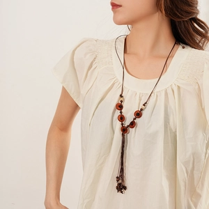 Close-up of Bohemian necklace with dark brown wooden beads and tassel on model