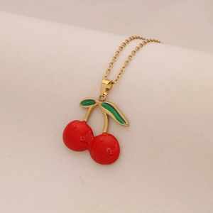 Collana con ciondolo a ciliegia dorata con frutti rossi e foglie verdi su tessuto