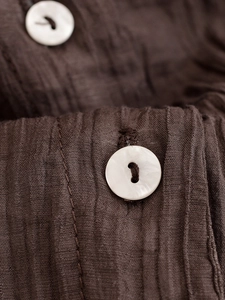 Makroaufnahme der braunen Crinkle-Stoffstruktur mit weißem Muschelknopf am Hemd