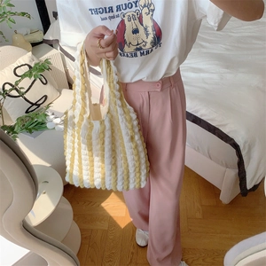 Detail of yellow and white bubble knit tote bag carried by hand in a home setting
