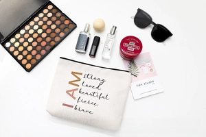 Flat lay of linen makeup bag with inspirational text surrounded by fashion items