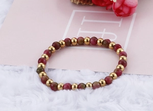 Macro detail of elastic beaded bracelet with gold beads and garnet stones on white fur