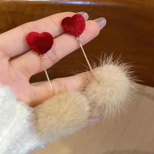 Détail de boucles d'oreilles pendantes avec cœur en velours rouge et pompon beige