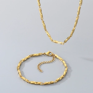 Close-up of golden stainless steel Chopin chain necklace and bracelet set on grey background