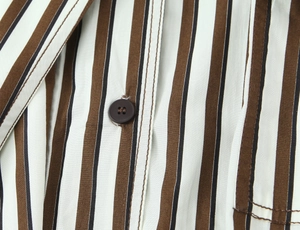 Dettaglio di camicia in cotone a righe con bottone in resina scura e cuciture precise