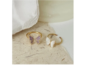 Detailed view of two butterfly rings featuring gold plating with purple and pearl finishes