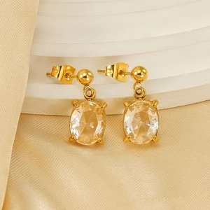 Boucles d'oreilles ovales en acier doré et zircon sur présentoir blanc et soie luxueuse
