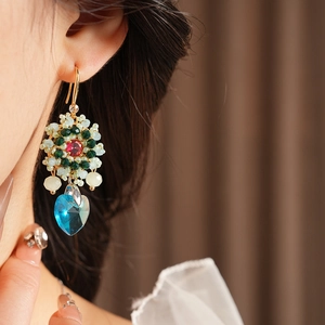 Dettaglio di orecchini vintage a fiore e cuore con perle verdi e cristallo blu su modella
