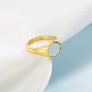 Close-up of golden geometric ring with a round shimmering shell inlay on white fabric