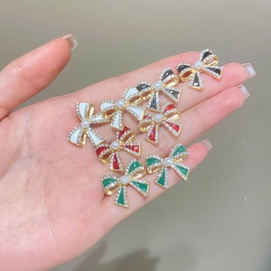 Close-up of glittery bow earrings with central pearl in red, green, black and white