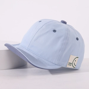 Close-up of cotton baby baseball cap with GOOD LUCKY tag and green smiley face detail