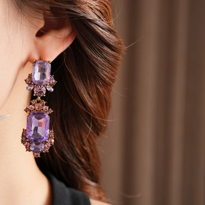Detail of vintage gold earrings with large purple rectangular and round gemstones on model