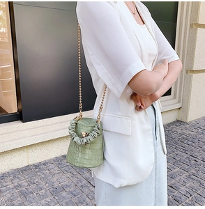 Close-up of green crocodile texture bucket bag with gold chain strap and pleated handle