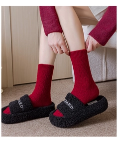 Detail of red cable-knit winter socks paired with black plush slippers and embroidery