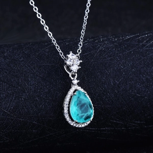 Macro shot of a teardrop paraiba blue pendant with white diamonds on black background