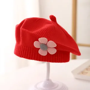 Detailed close-up of a red knit beret for girls featuring a 3D floral accent on a stand