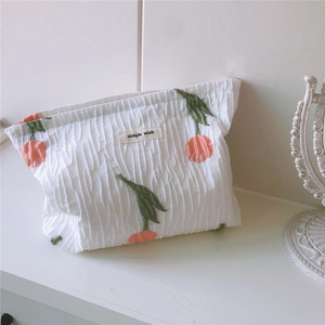 Détails de broderie de tulipe et texture plissée sur une trousse de maquillage blanche