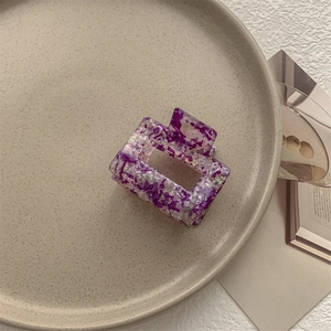 Dettaglio di una pinza per capelli rettangolare viola marmorizzata su un piatto di ceramica