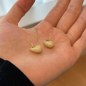 Close-up of gold pear-shaped stud earrings with pavé white zircons on hand