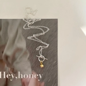 S-shaped 925 silver necklace with golden bell pendant and OT clasp on a magazine background