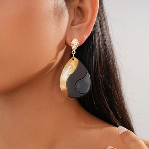 Close-up of a large teardrop earring with irregular geometric patterns in gold and brown