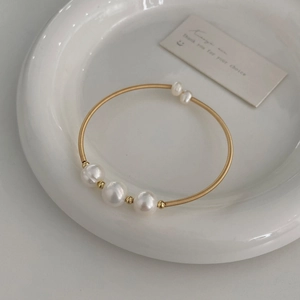 Detail of gold-plated open bangle featuring five natural freshwater pearls on a white dish