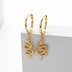 Macro shot of gold snake drop earrings on a white stand showing detailed metallic texture